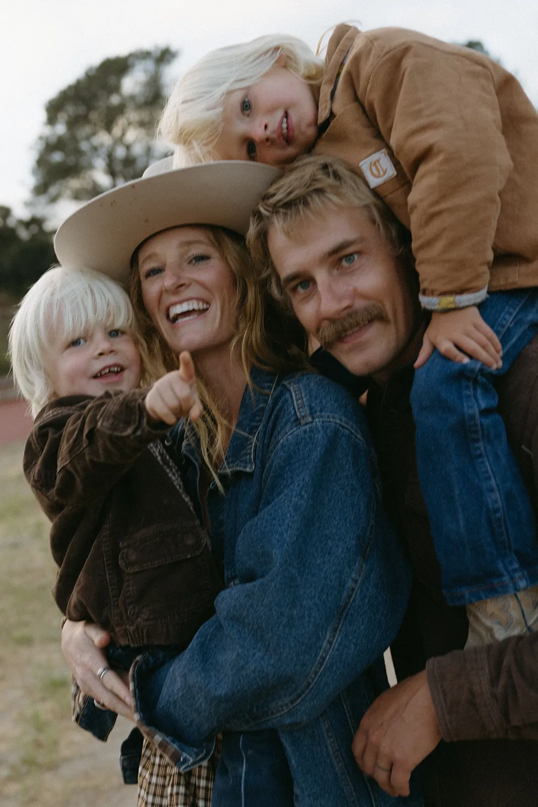 A family pressed cheek to cheek, laughing, the youngest on his father’s shoulders