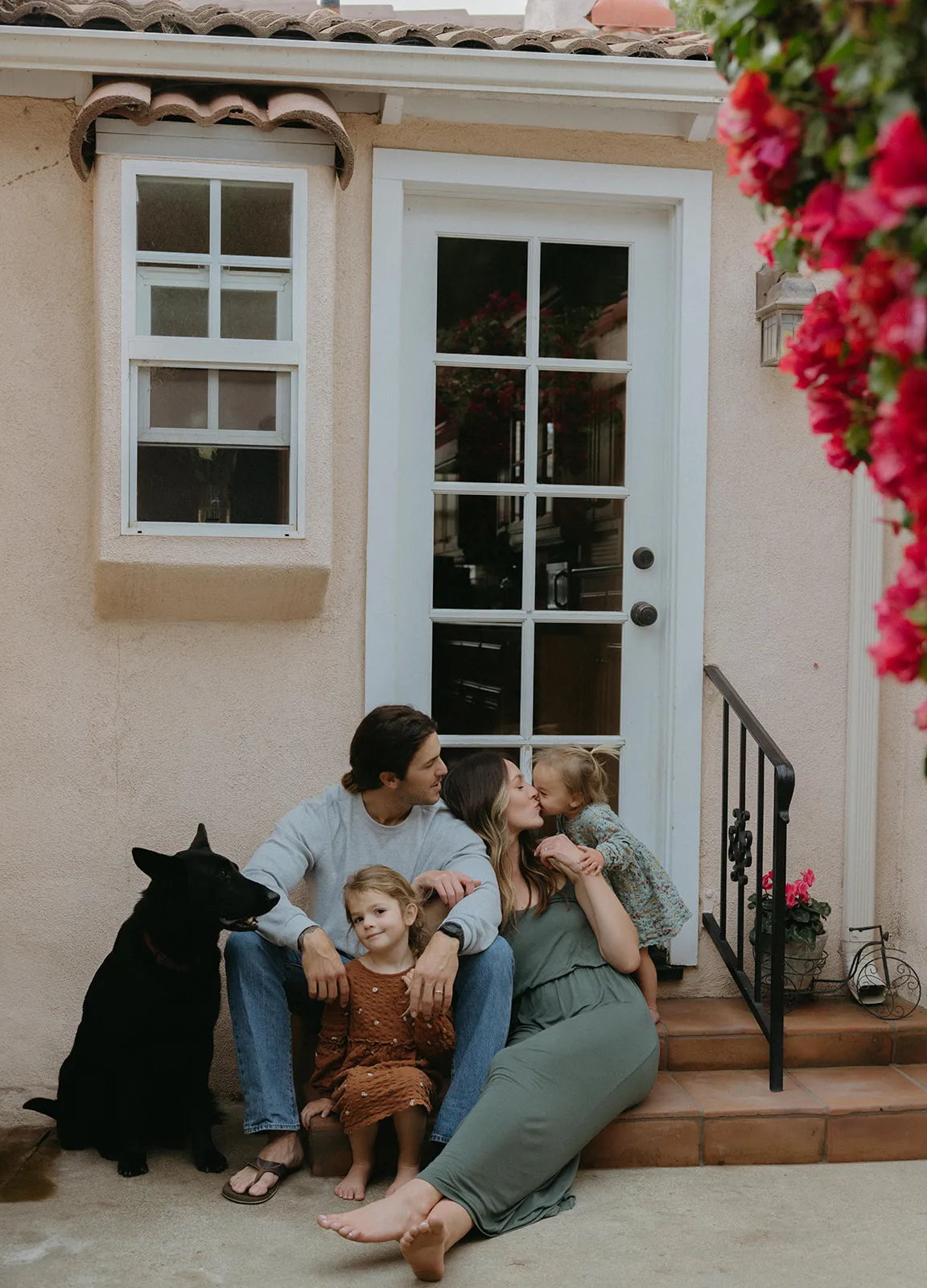 A family sitting on their front steps with their dog